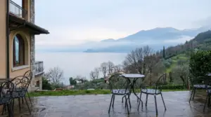 Vista sul Lago di Garda da una terrazza con tavoli e sedie in ferro battuto in una giornata nuvolosa
