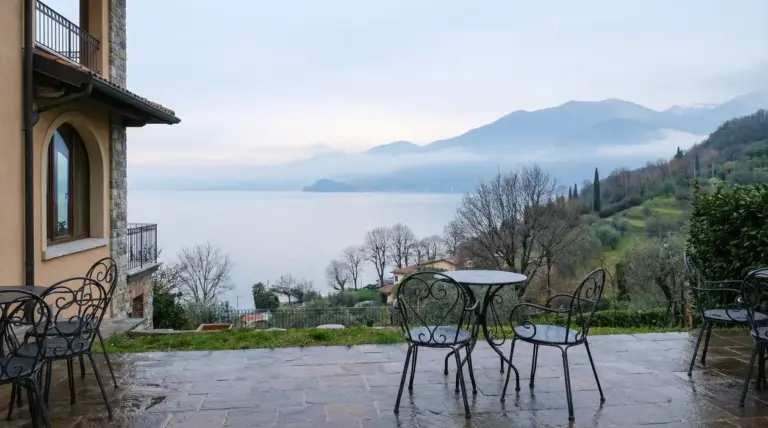 Vista sul Lago di Garda da una terrazza con tavoli e sedie in ferro battuto in una giornata nuvolosa